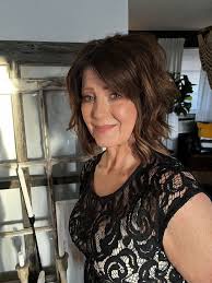A woman with shoulder-length brown hair, wearing a black lace top, smiles slightly at the camera.