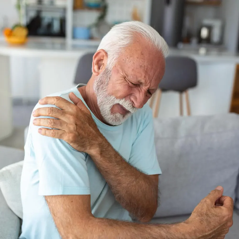 Elderly man grimacing and holding his shoulder in pain.