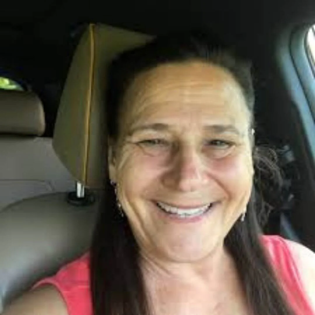 Person smiling inside a car, wearing a pink top.