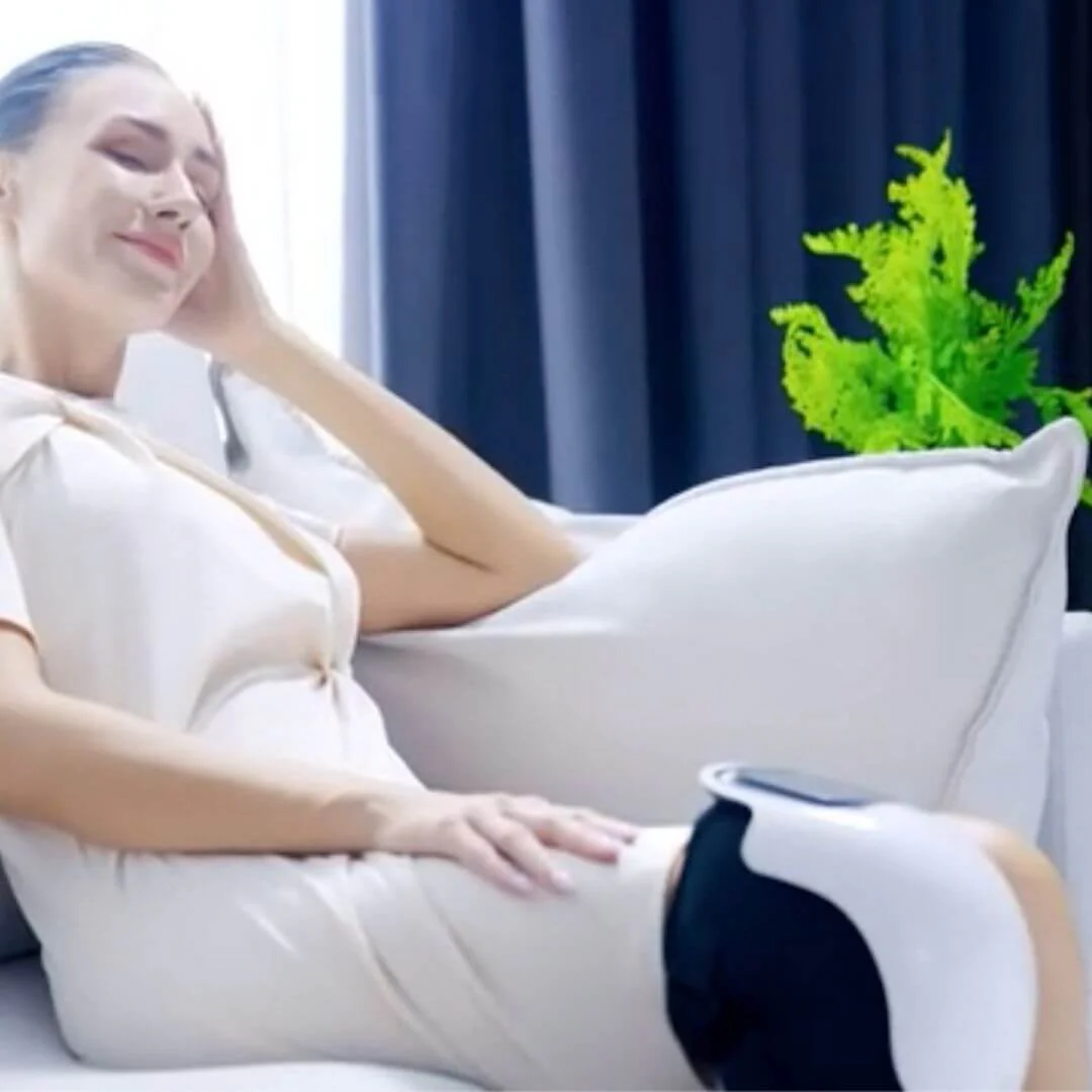 Woman relaxing on a couch with a knee massager, plant in background.