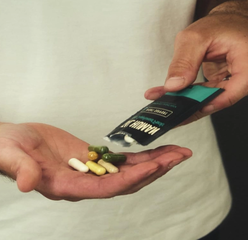 A person pouring several colorful capsules from a small black packet into their cupped hand.