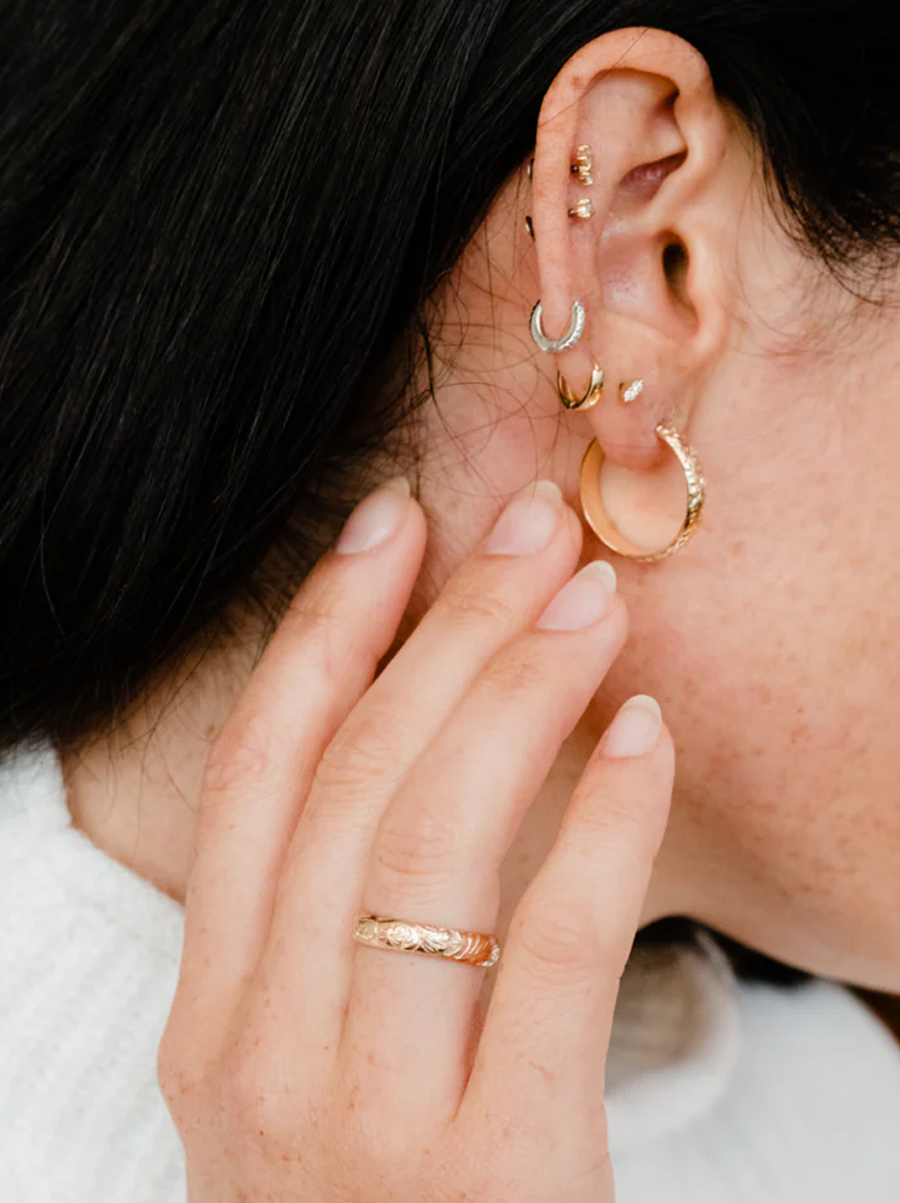 Close-up of an ear with multiple earrings and a hand with a ring.