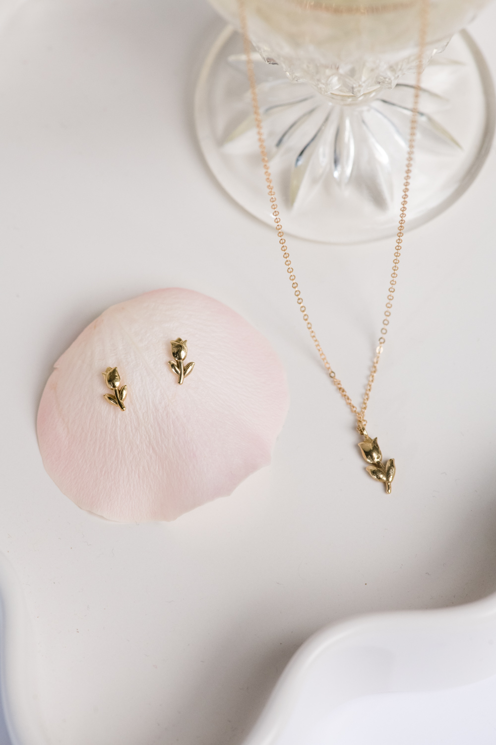 A pink rose with gold and pink necklaces hanging from its stem.