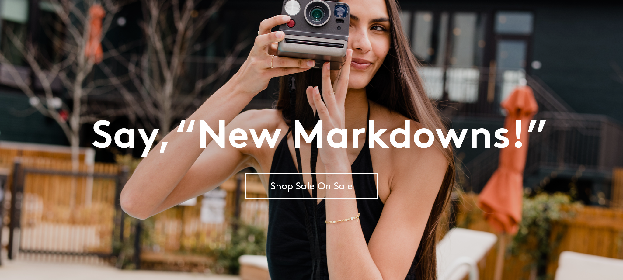 Woman outside taking a photo with a vintage camera and black halter dress on, text reads say, new markdowns shop sale on sale