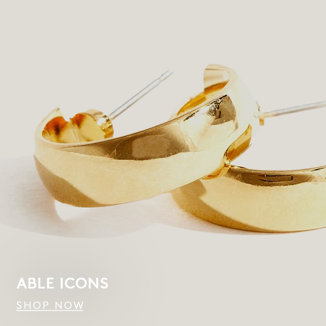 Close-up of two gold hoop earrings on a light background. text reads able icons, shop now