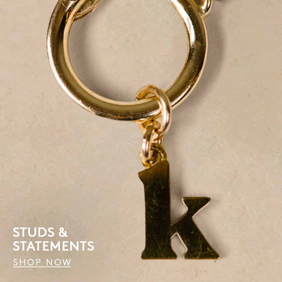 gold letter k initial charm on a small gold hoop, text reads studs and statements, shop now