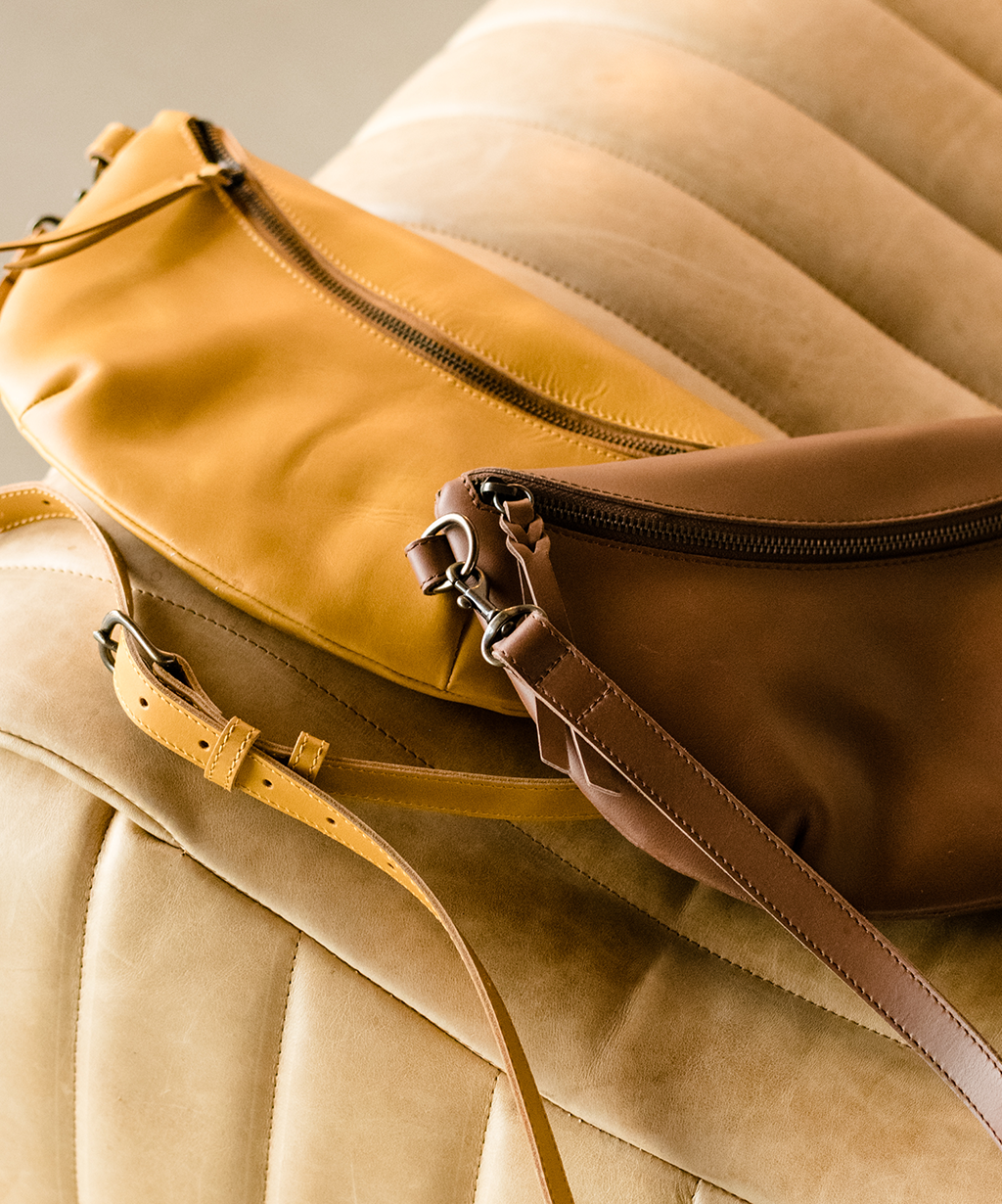 Two leather bags, one brown and one tan, on a beige cushioned surface.