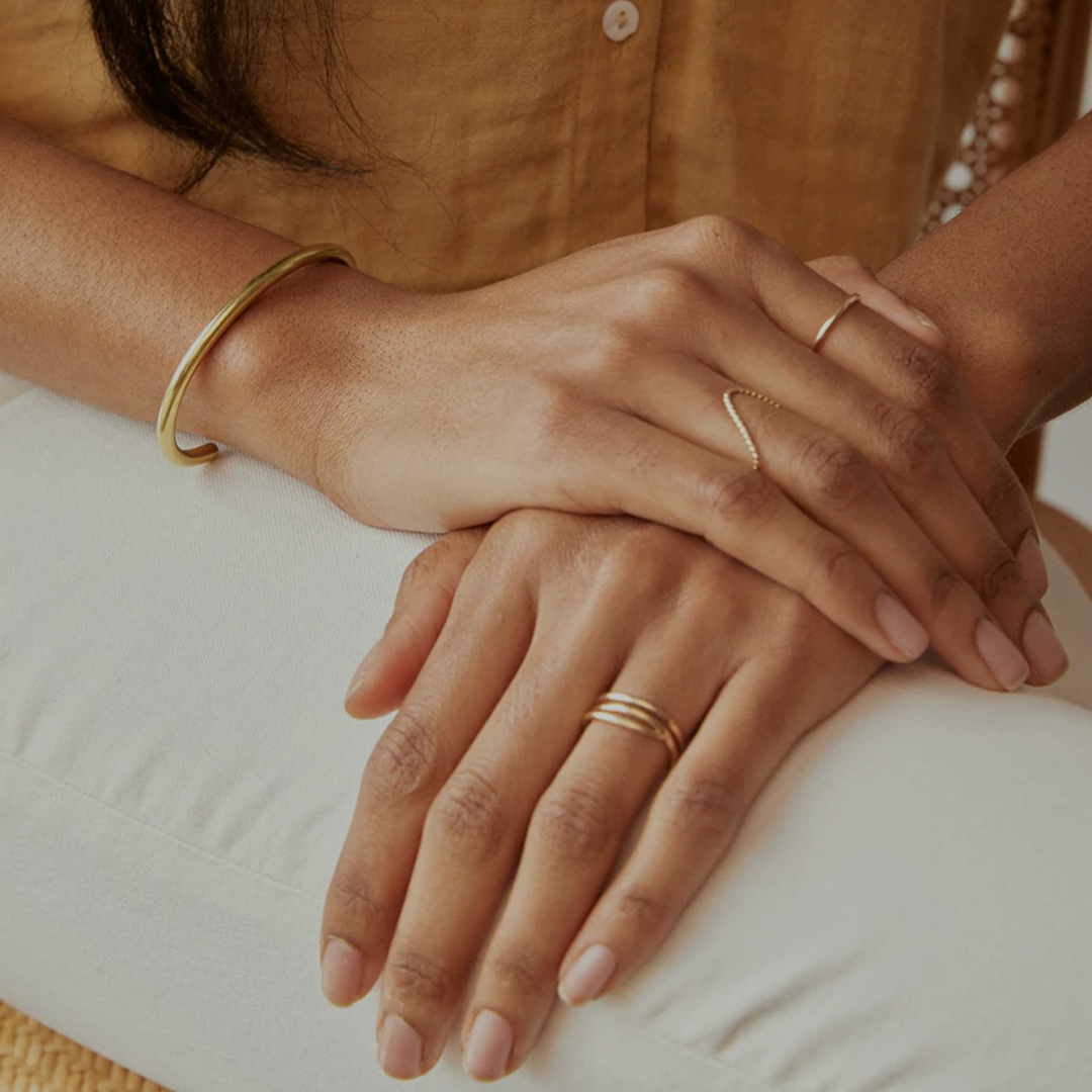 Close-up of hands with gold rings and bracelet on a lap.