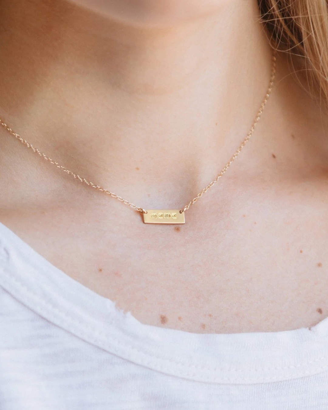 Gold necklace with 'mama' engraved on a rectangular pendant.