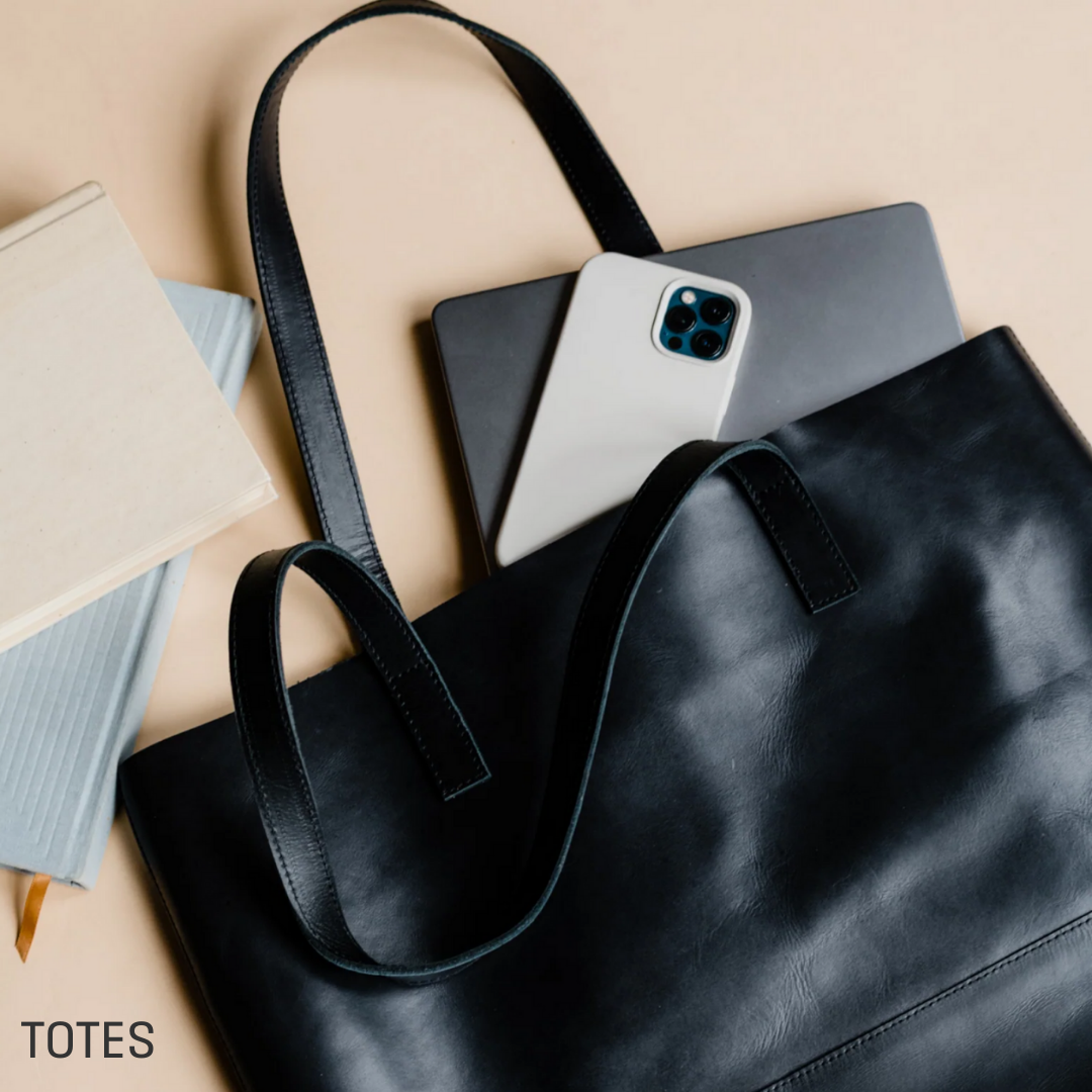 Black tote bag with a phone and laptop partially inside. SHOP TOTES