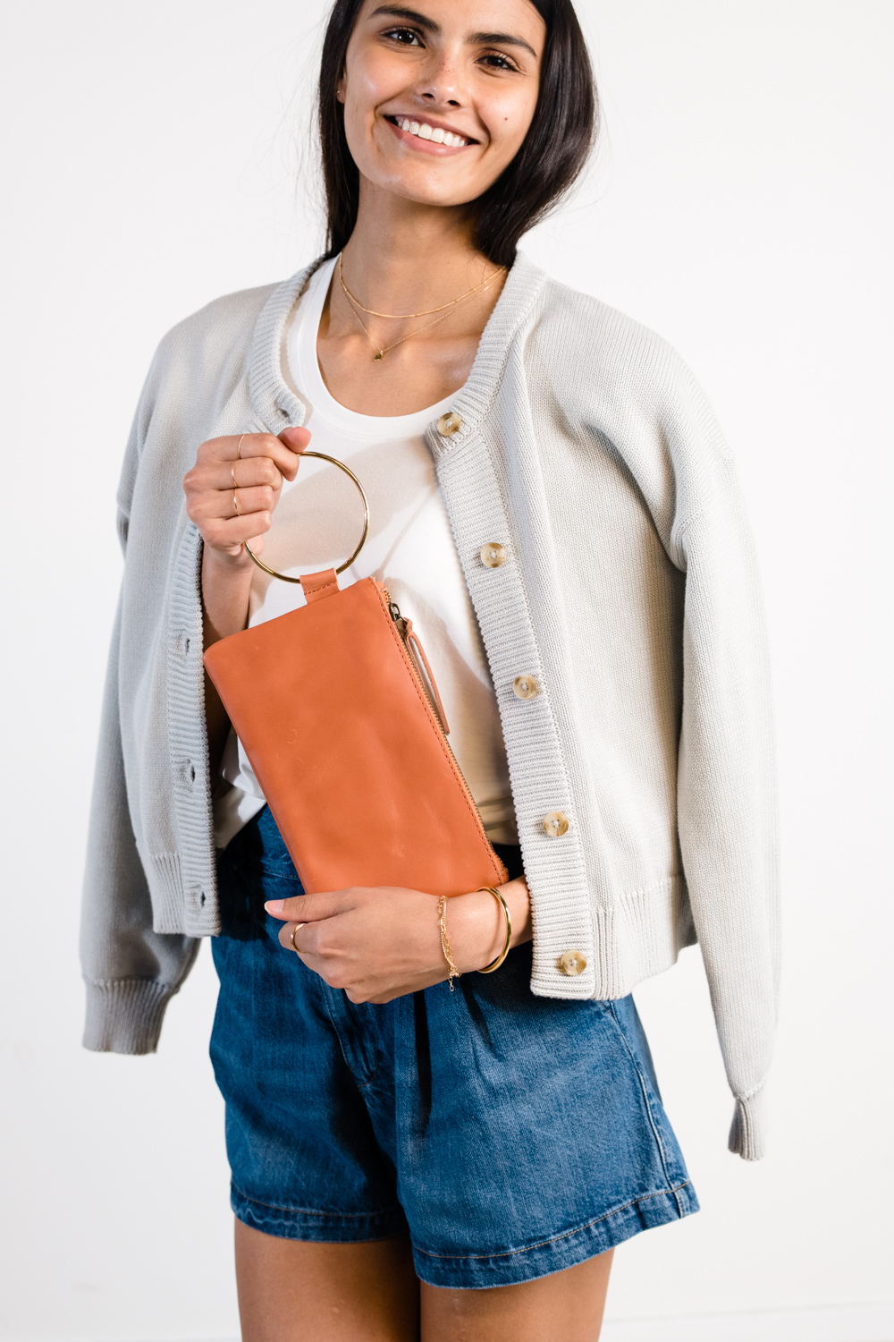 Smiling person holding a brown clutch with a gold ring handle.