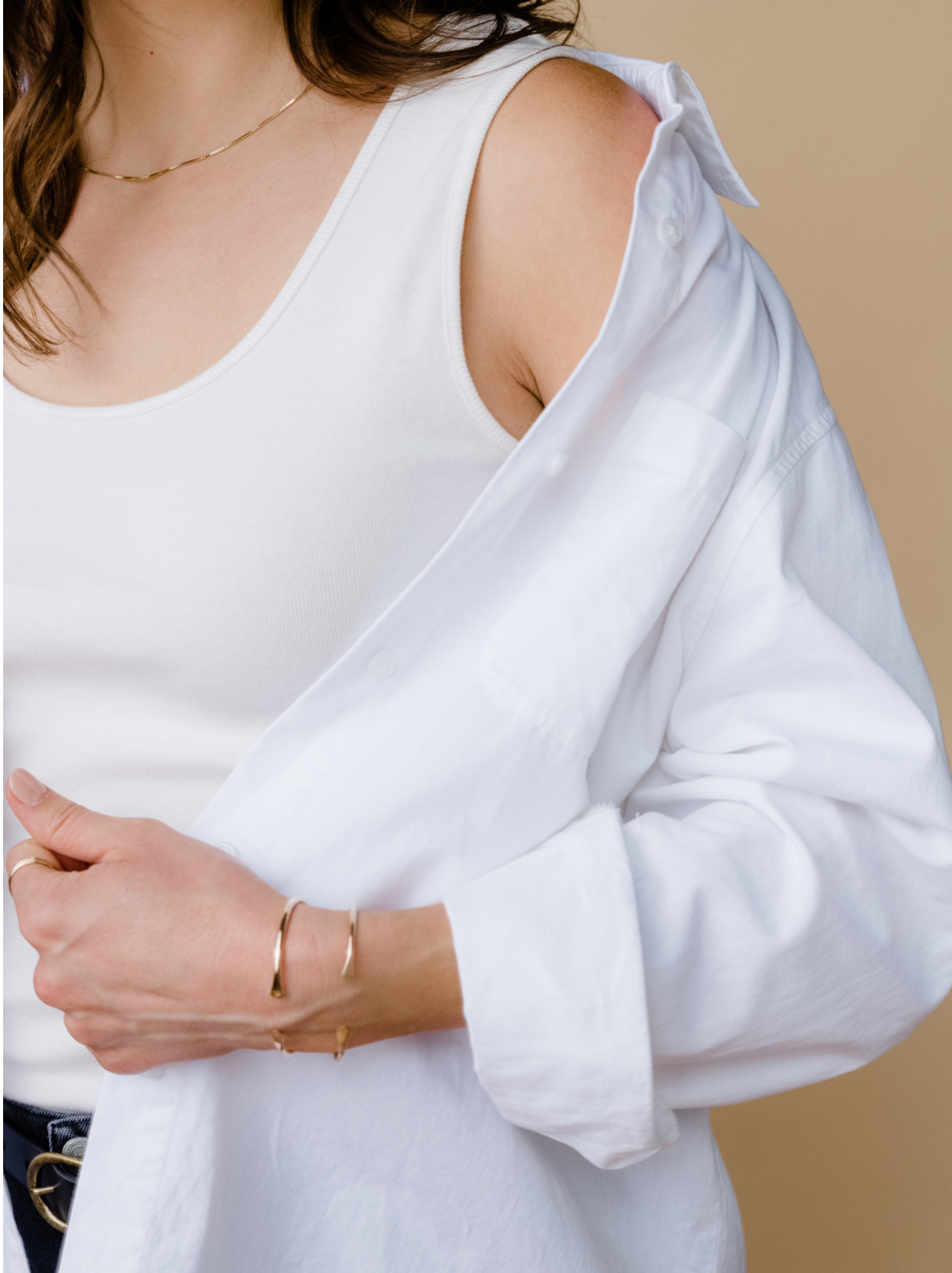Person wearing white tank top, open white shirt, and gold jewelry.