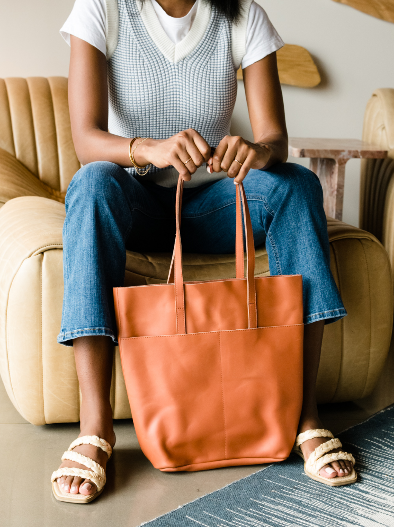 Person seated with a tan tote bag and wearing jeans and sandals.