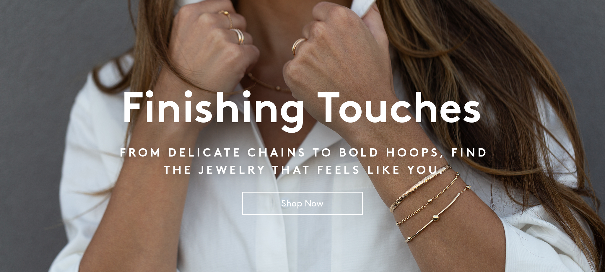 Woman wearing a bracelet stack and rings with hands holding the collar of her white button down shirt. text reads finishing touches. from delicate chains to bold hoops, find the jewelry that feels like you. shop now button.