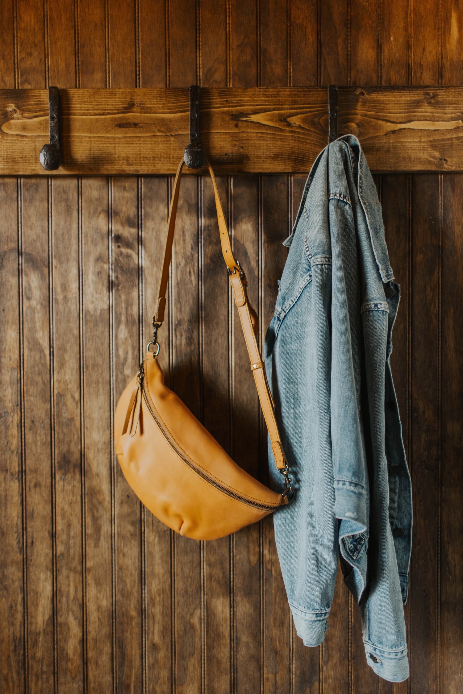 Tan leather bag and denim jacket on wooden hooks.