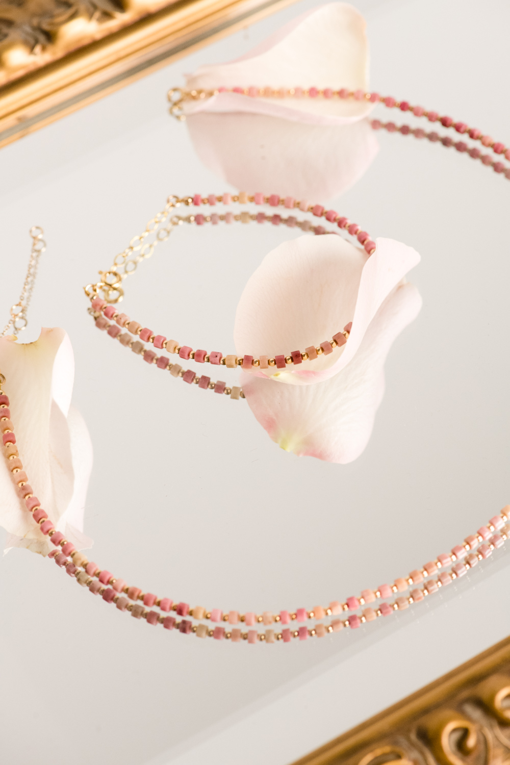 Pink bead necklace and bracelet on a mirrored surface with rose petals.