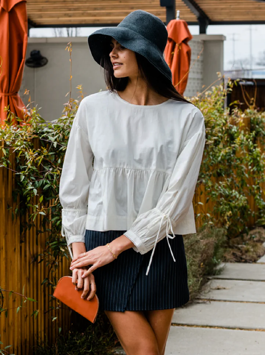 Woman in white blouse and black hat holding a small orange clutch.