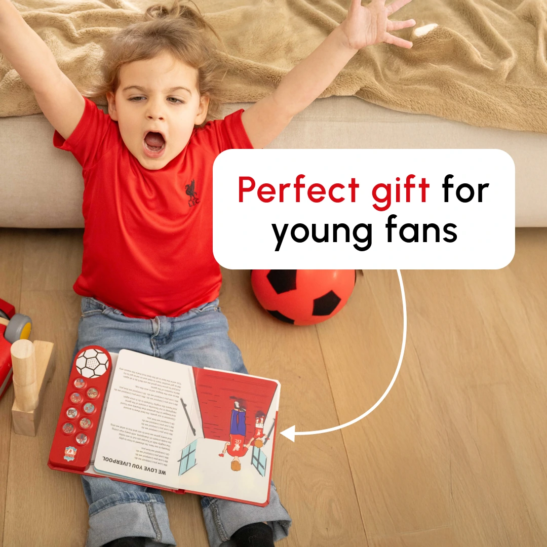 Child in red shirt with open book and soccer ball on the floor.