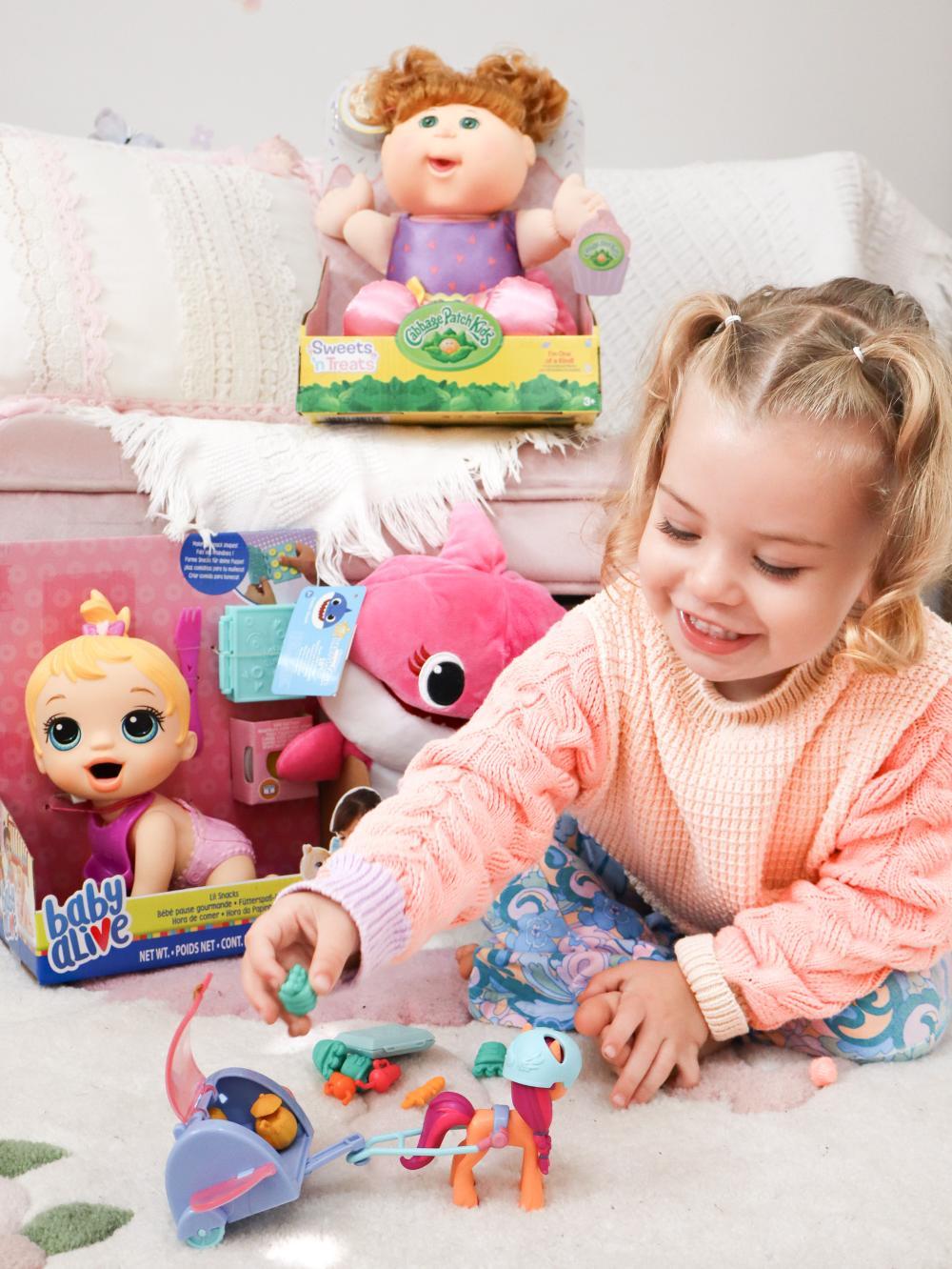 Child playing with toys, including dolls and a small colorful animal figure.