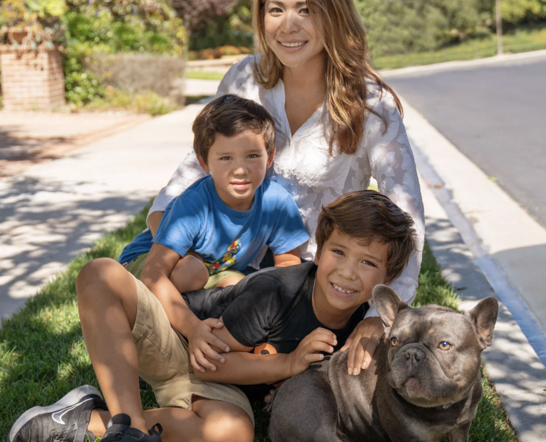 Two children and a woman sitting with a dog on the grass.