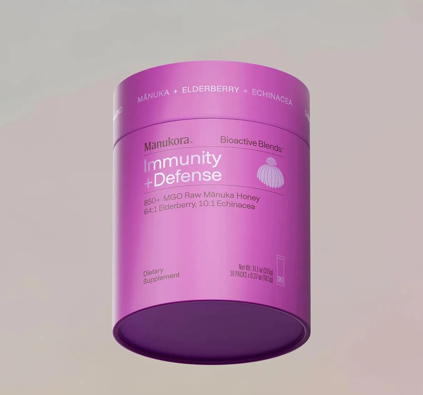 A pink and purple cylindrical container of Manukora Immunity + Defense dietary supplement floating against a neutral background.