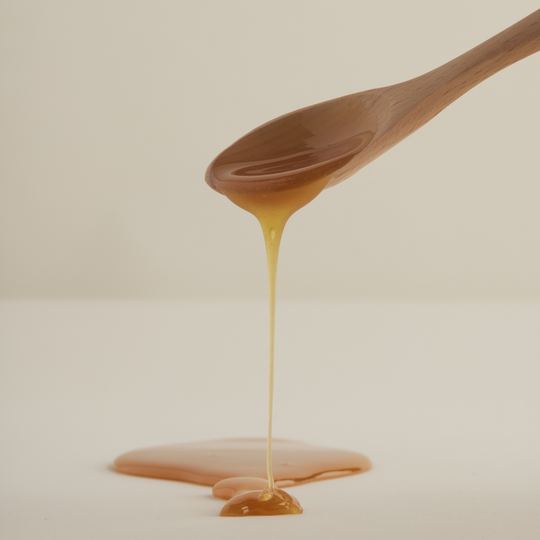 Wooden spoon with honey dripping onto a white surface.