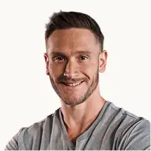 A headshot of a smiling man with short brown hair and a beard, wearing a grey t-shirt.