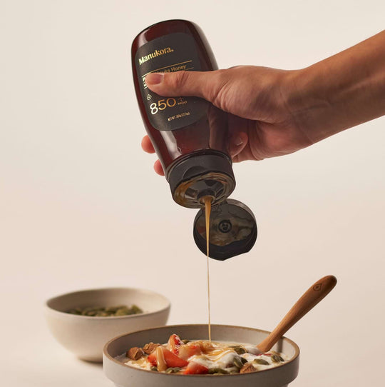 Hand pouring honey from a bottle onto a bowl of food.