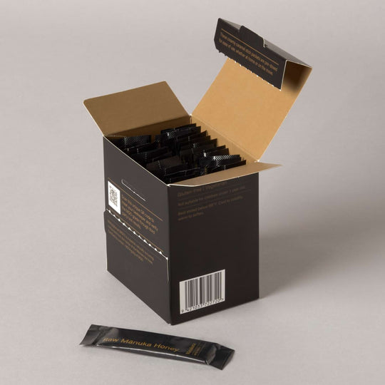 Open box of black honey packets on a gray background.
