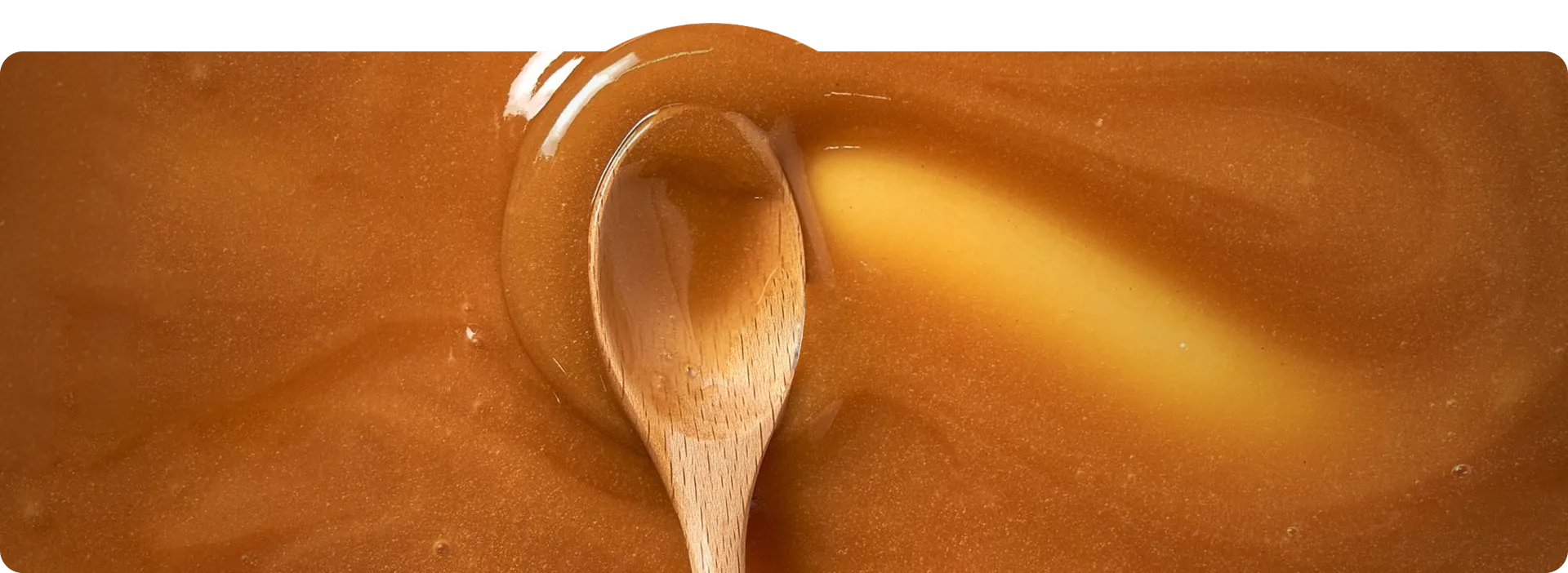 A wooden spoon swirling in a pool of golden, glossy caramel.