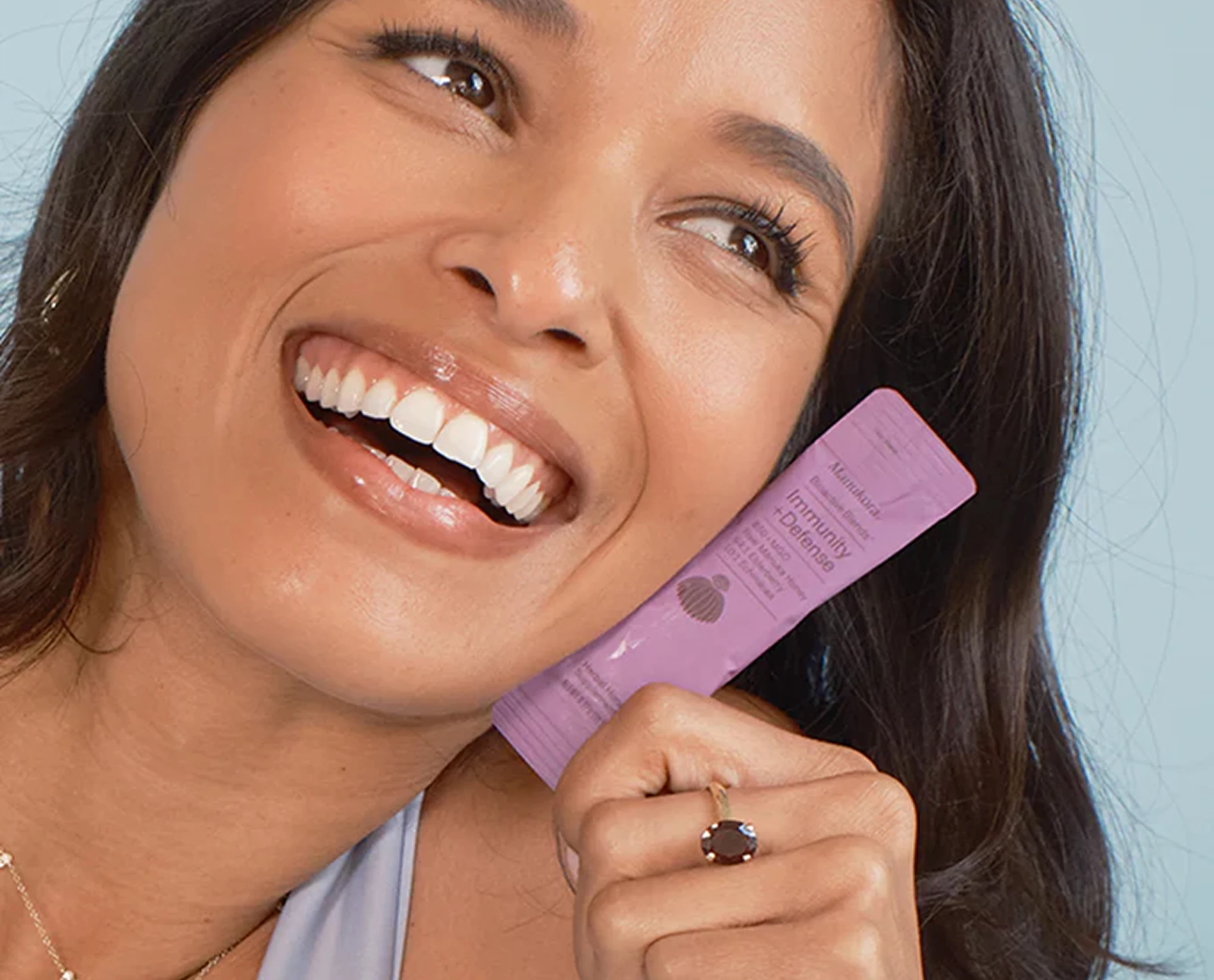 A smiling woman holds a purple 'Immunity + Defense' supplement packet.