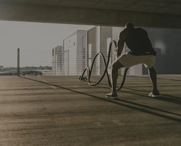 A man from behind exercises with battle ropes in what appears to be a parking garage.