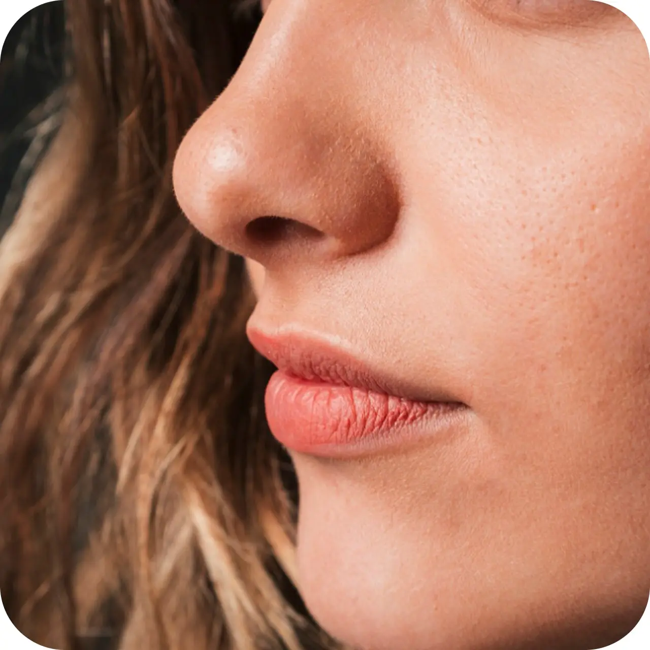 Close-up of a person's nose and lips with wavy brown hair.