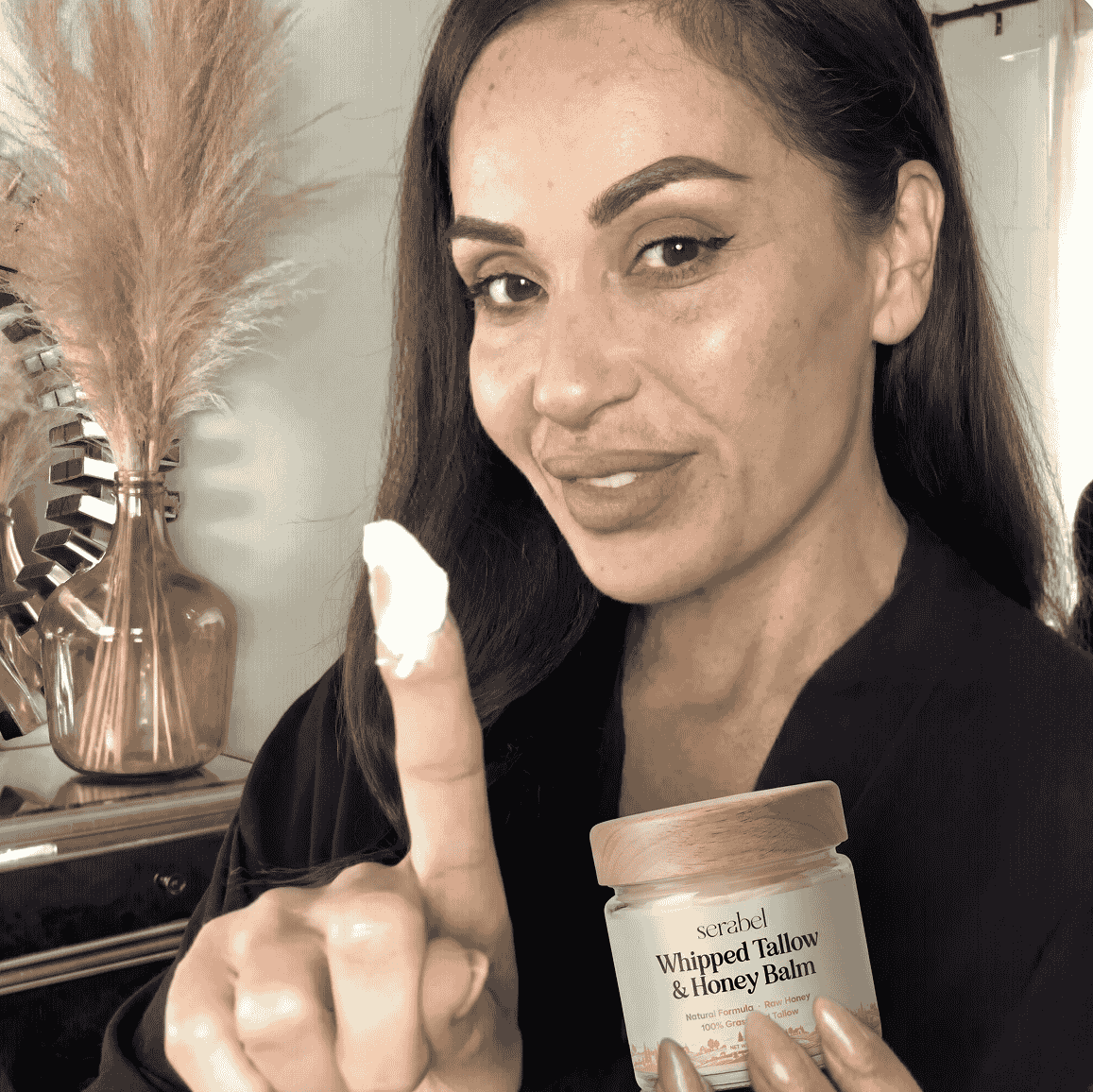 A woman holds up a finger with cream on it while holding a jar of Serabel beauty balm.