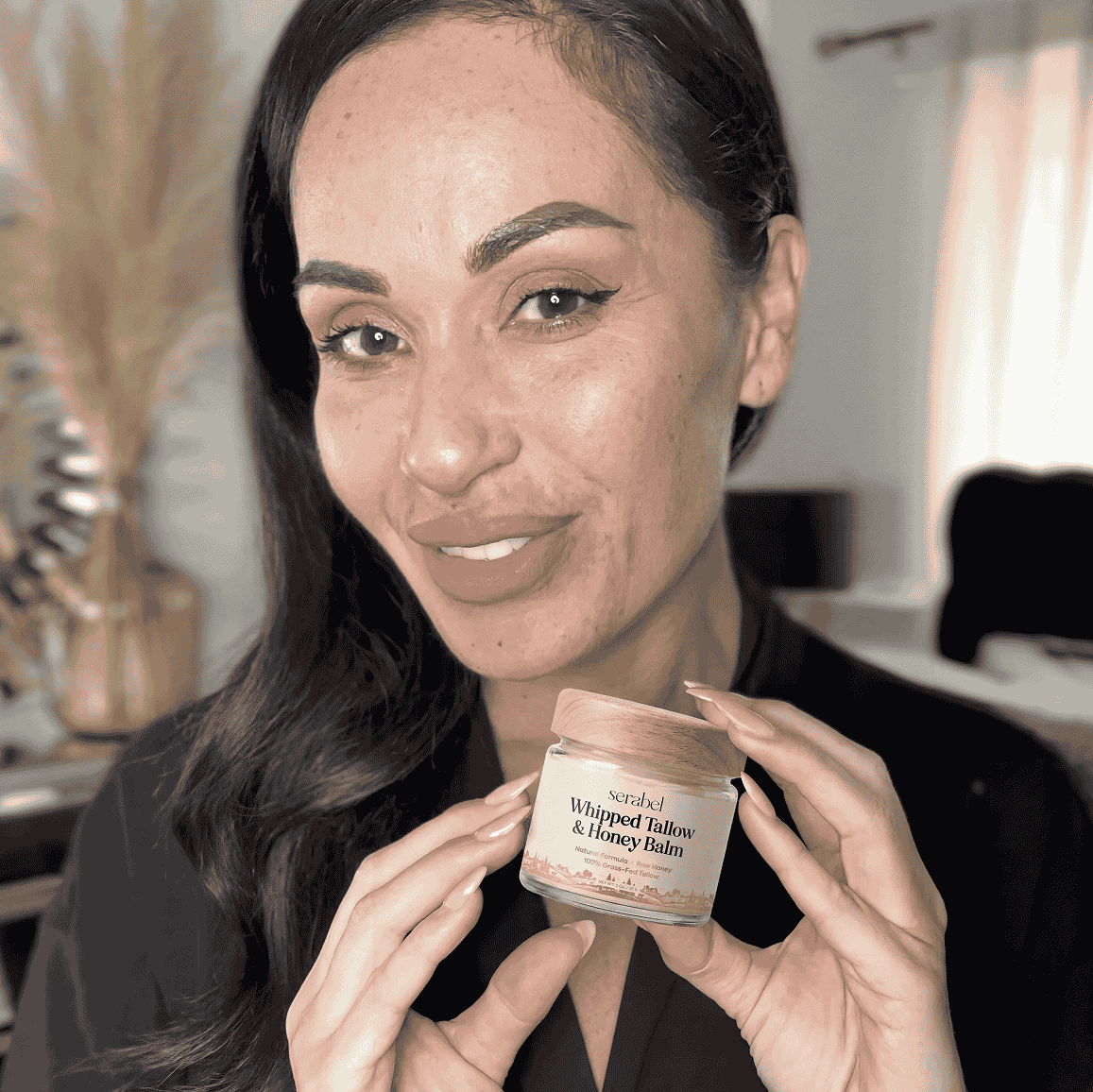 A smiling woman holds up a small jar of Serabel Whipped Tallow & Honey Balm.