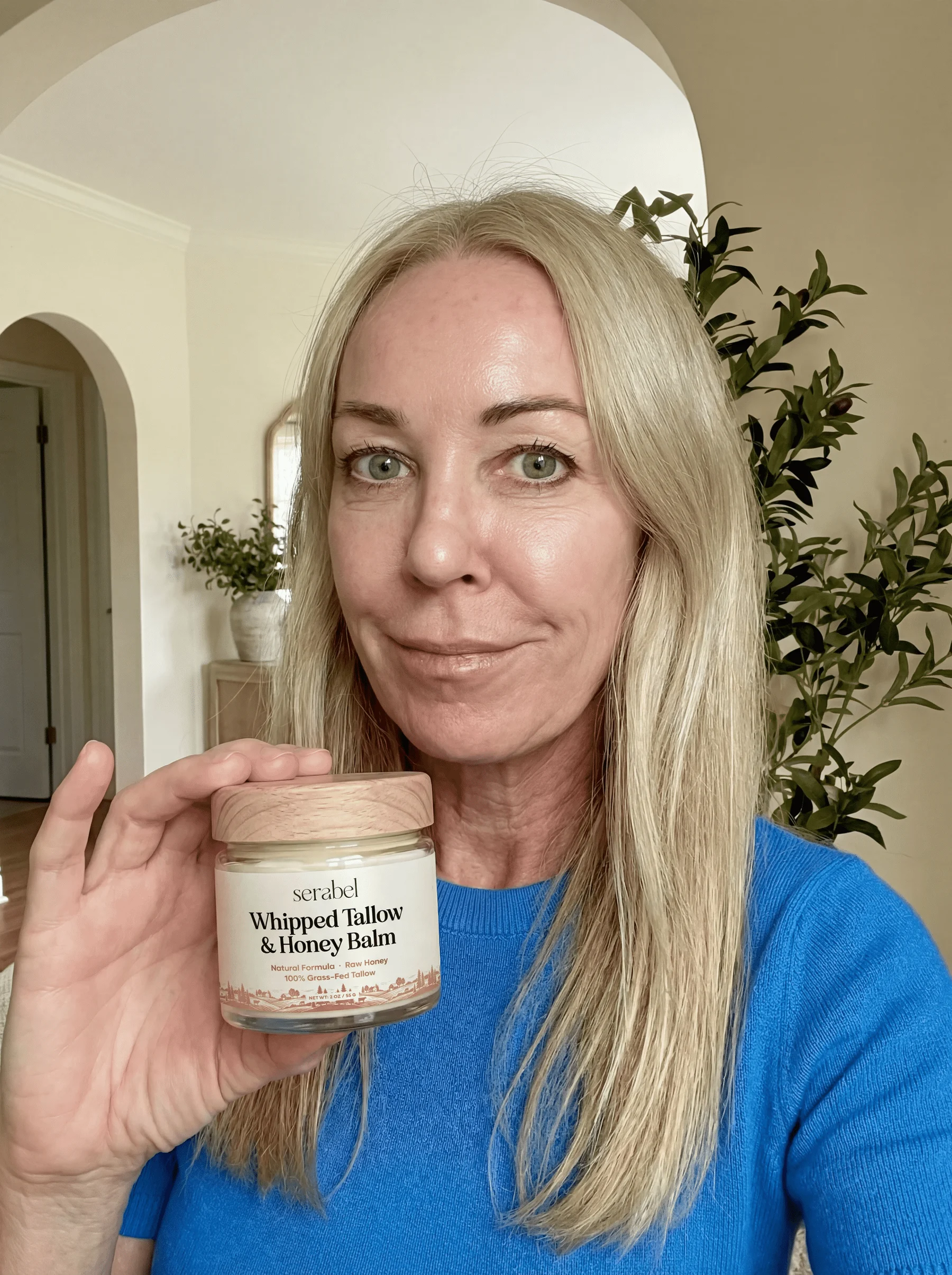 A woman with blonde hair holds a jar of Serabel Whipped Tallow & Honey Balm.