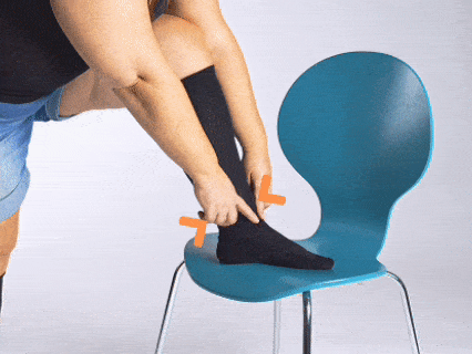Person using a sock aid to put on black socks while seated on a blue chair.