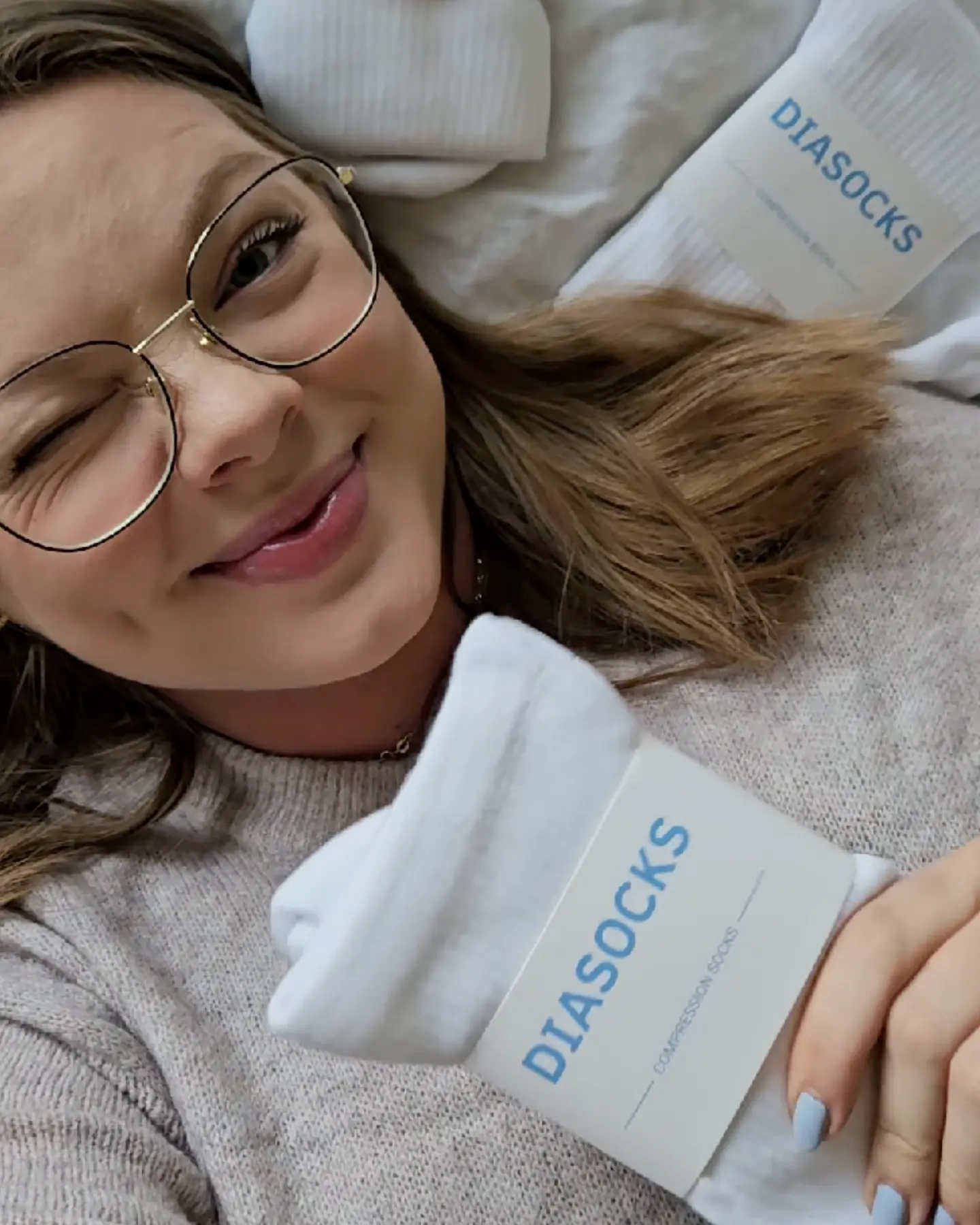 Person winking, holding white socks labeled 'DIASOCKS' with a smile.