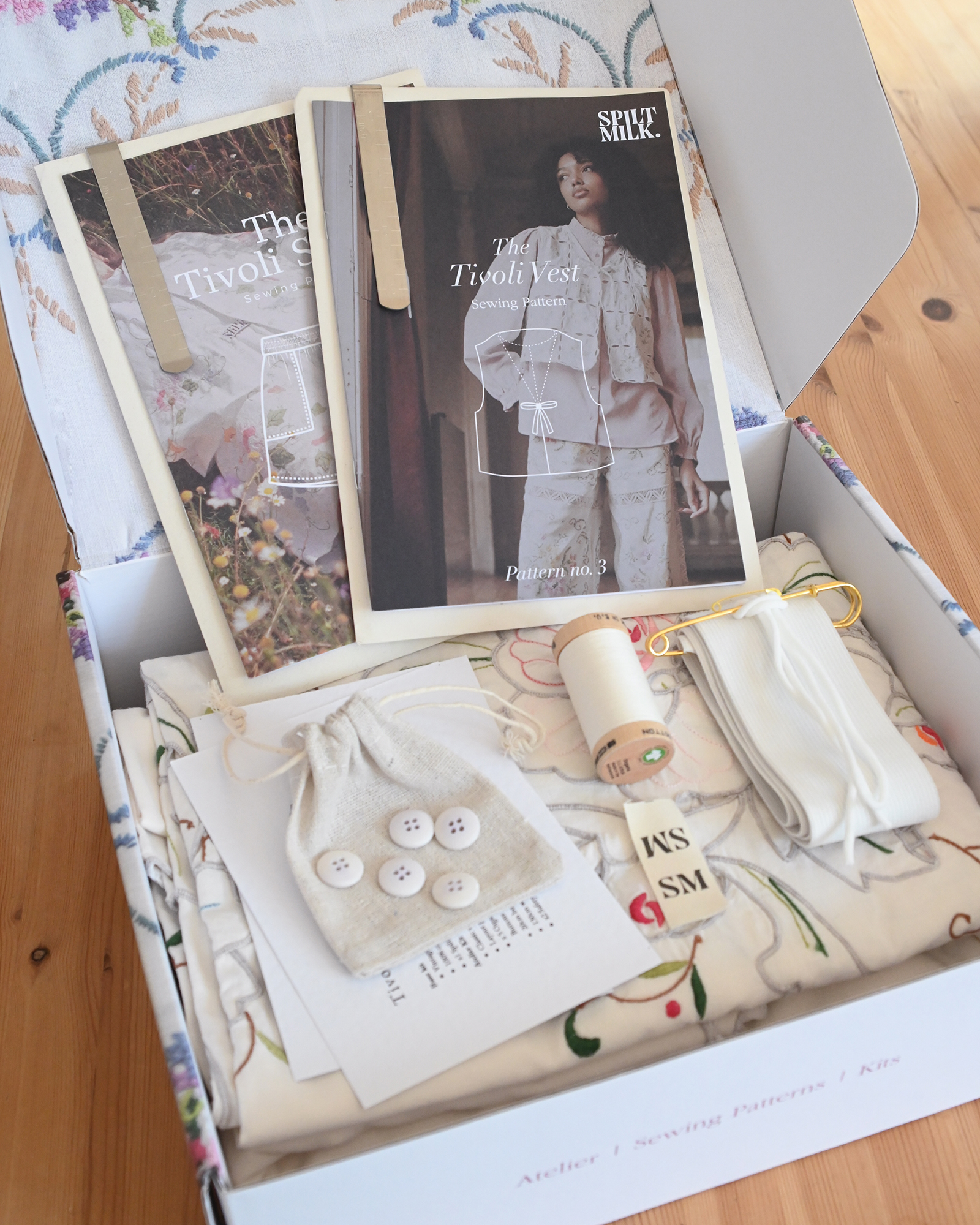 An open box showing the contents of a sewing kit, including patterns, fabric, buttons, and thread.