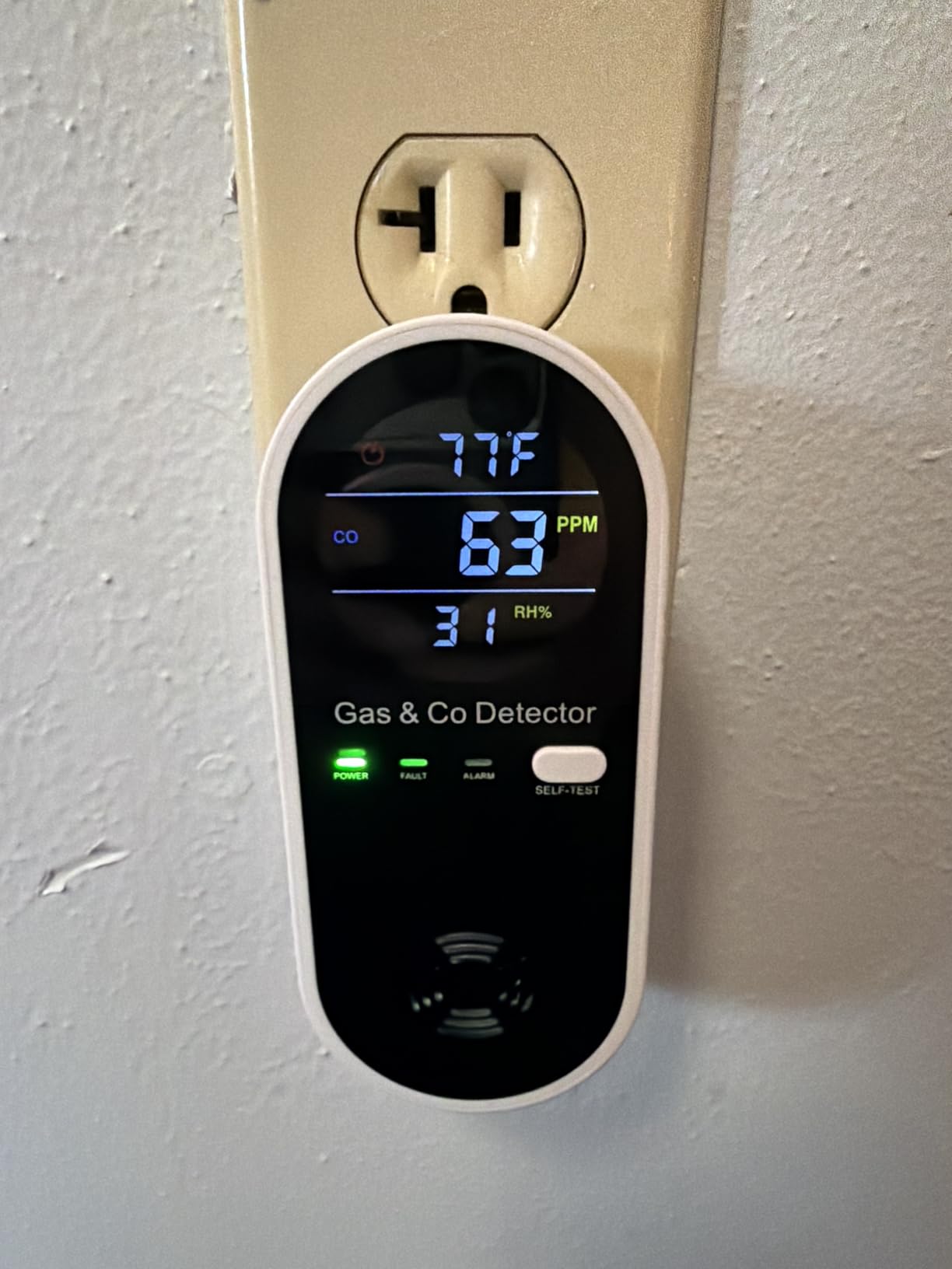 A digital gas and carbon monoxide detector plugged into a wall outlet displaying a CO reading of 63 PPM.
