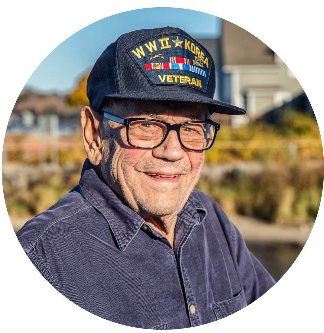 Elderly man wearing a 'WWII Korea Veteran' cap, smiling outdoors.