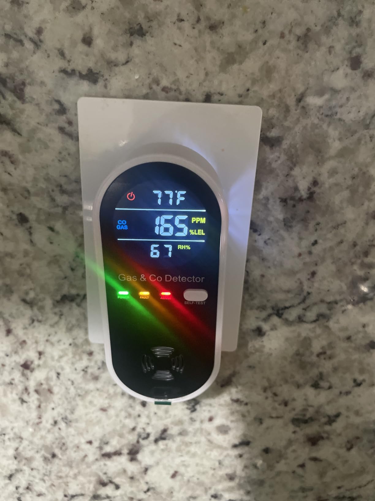 A plug-in gas and carbon monoxide detector with its digital display on, showing environmental readings.