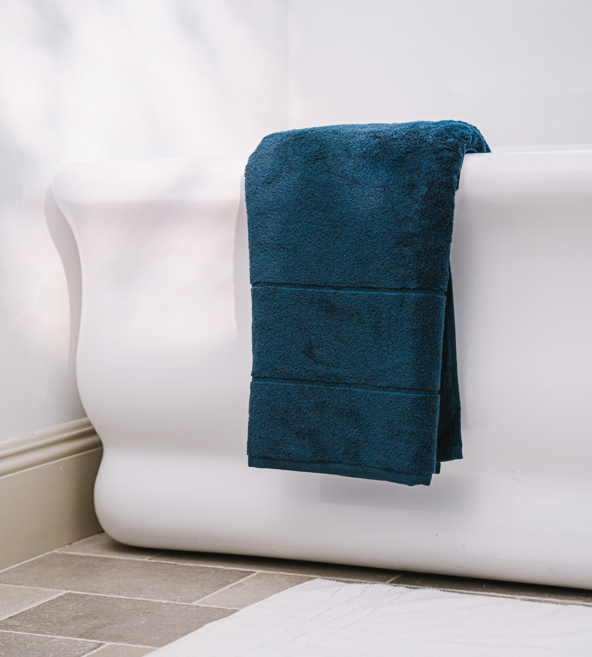 A dark blue towel is draped over the side of a white bathtub on a tiled floor.