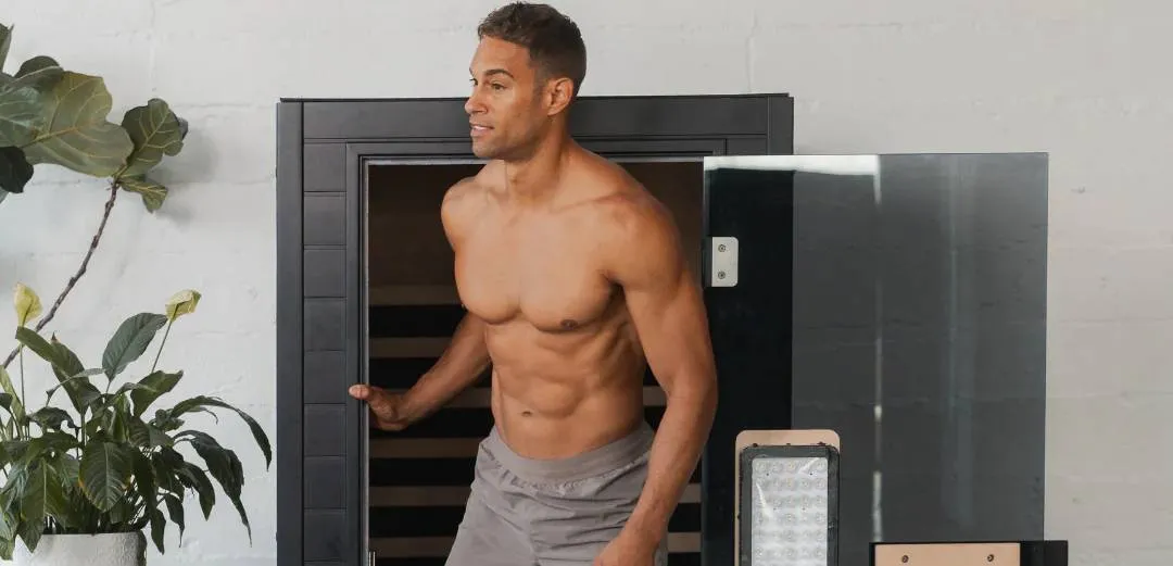 Person sitting in a wooden sauna with eyes closed, wearing workout clothes.