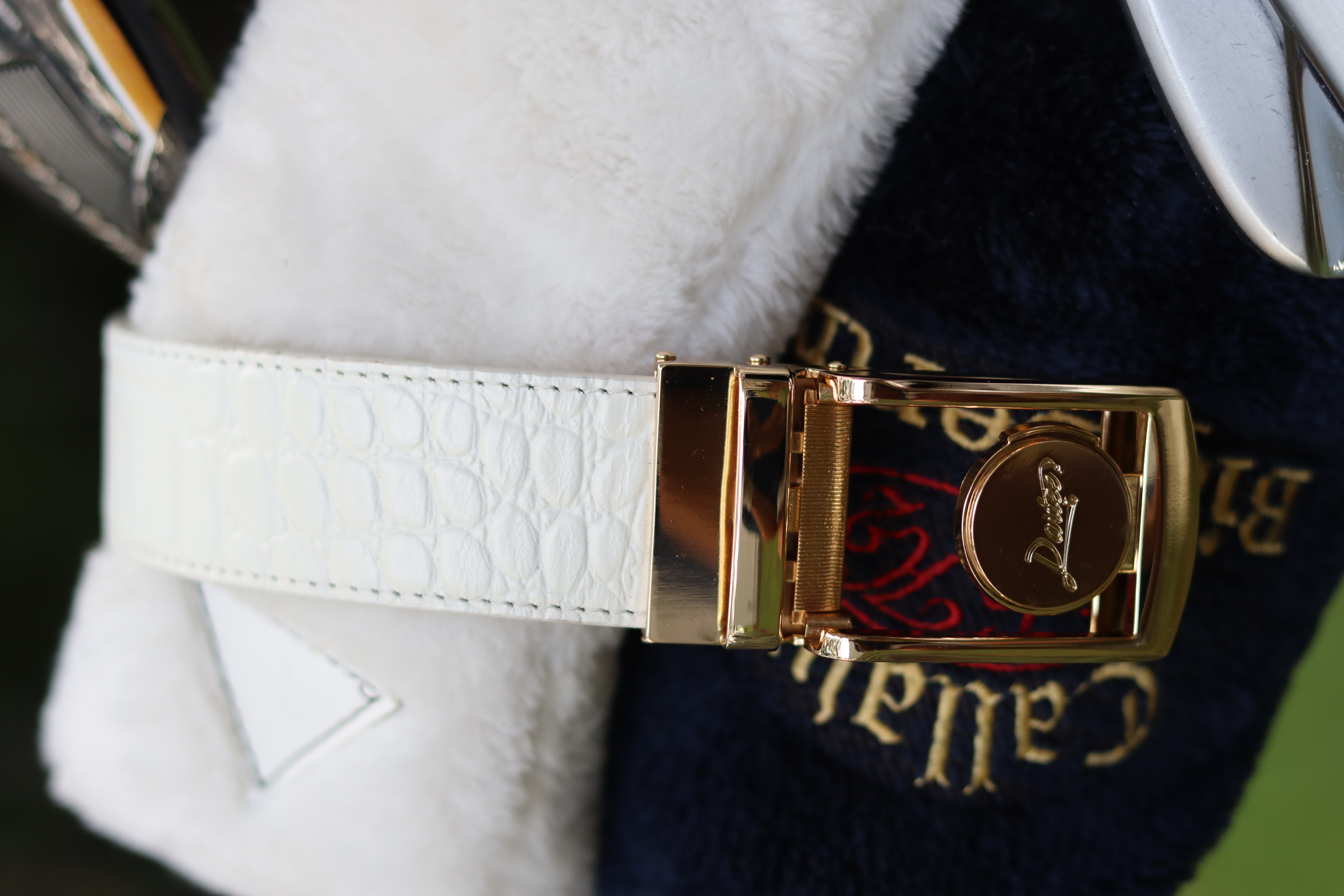 Close-up of a gold buckle on a white textured strap with embroidered text.