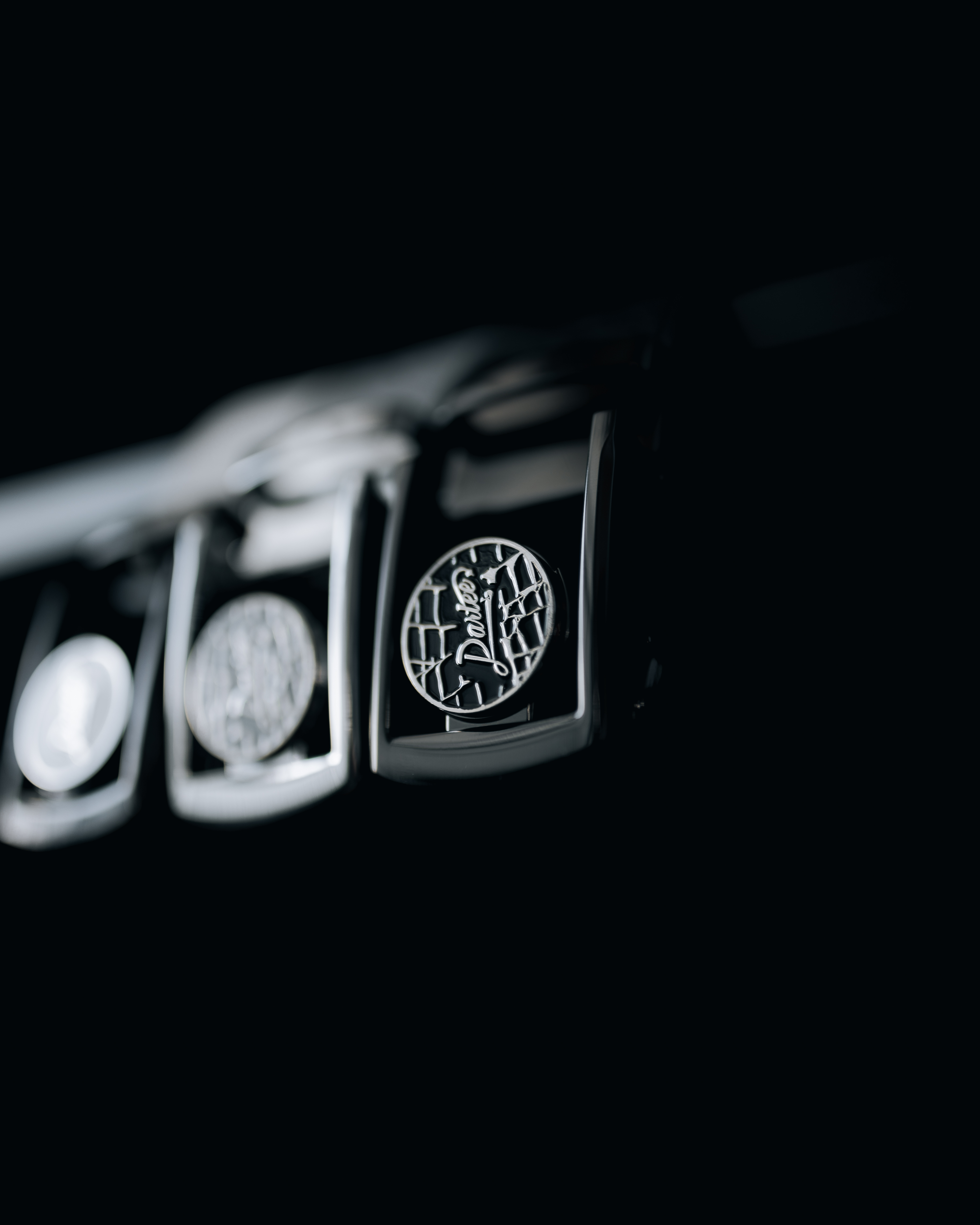 A close-up, selective focus shot of a chrome emblem with a script logo against a black background.