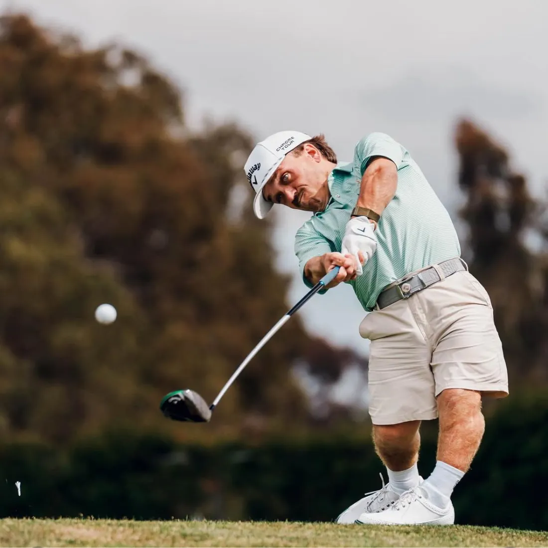 Person swinging a golf club on a golf course.