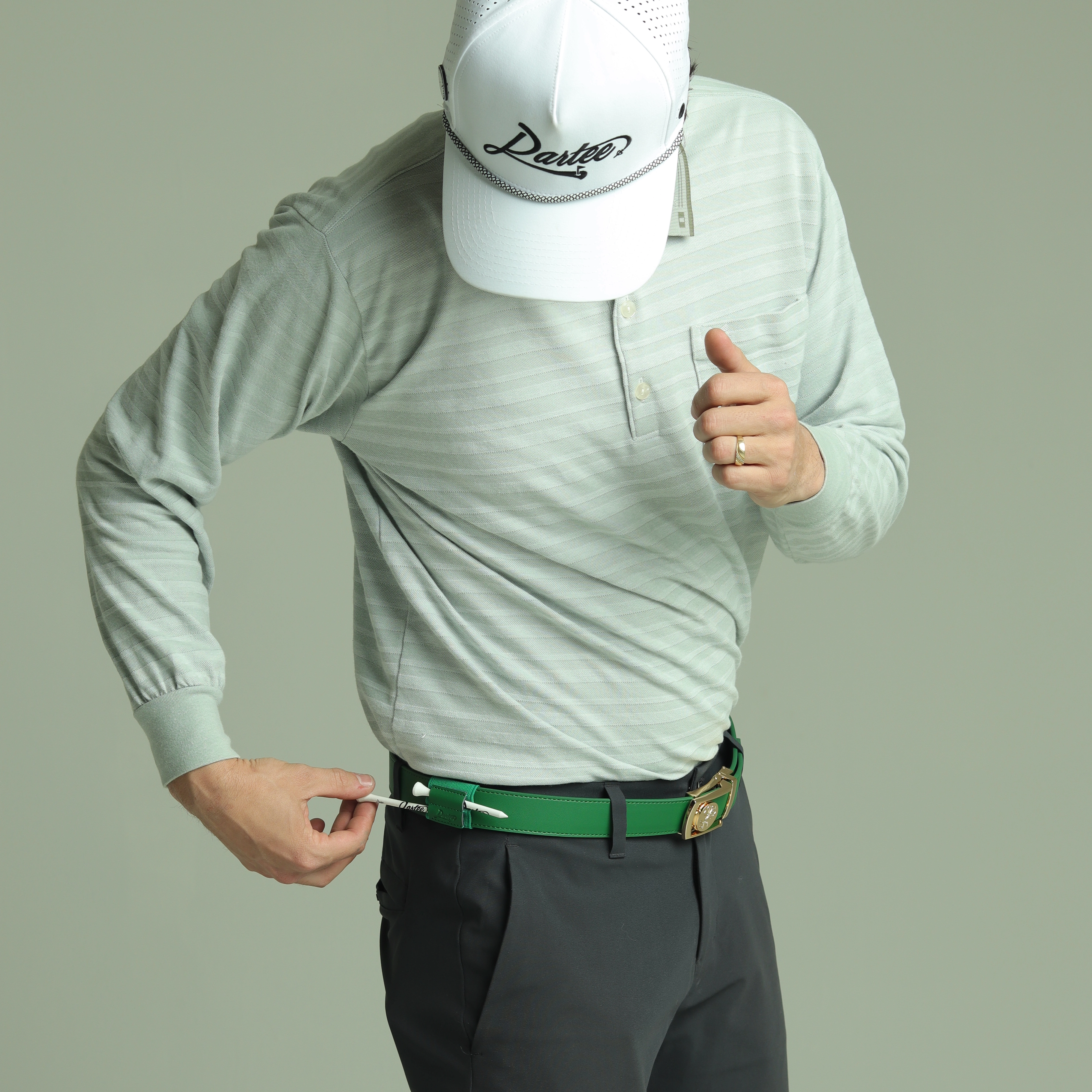 Person adjusting a green belt, wearing a cap and light long-sleeve shirt.