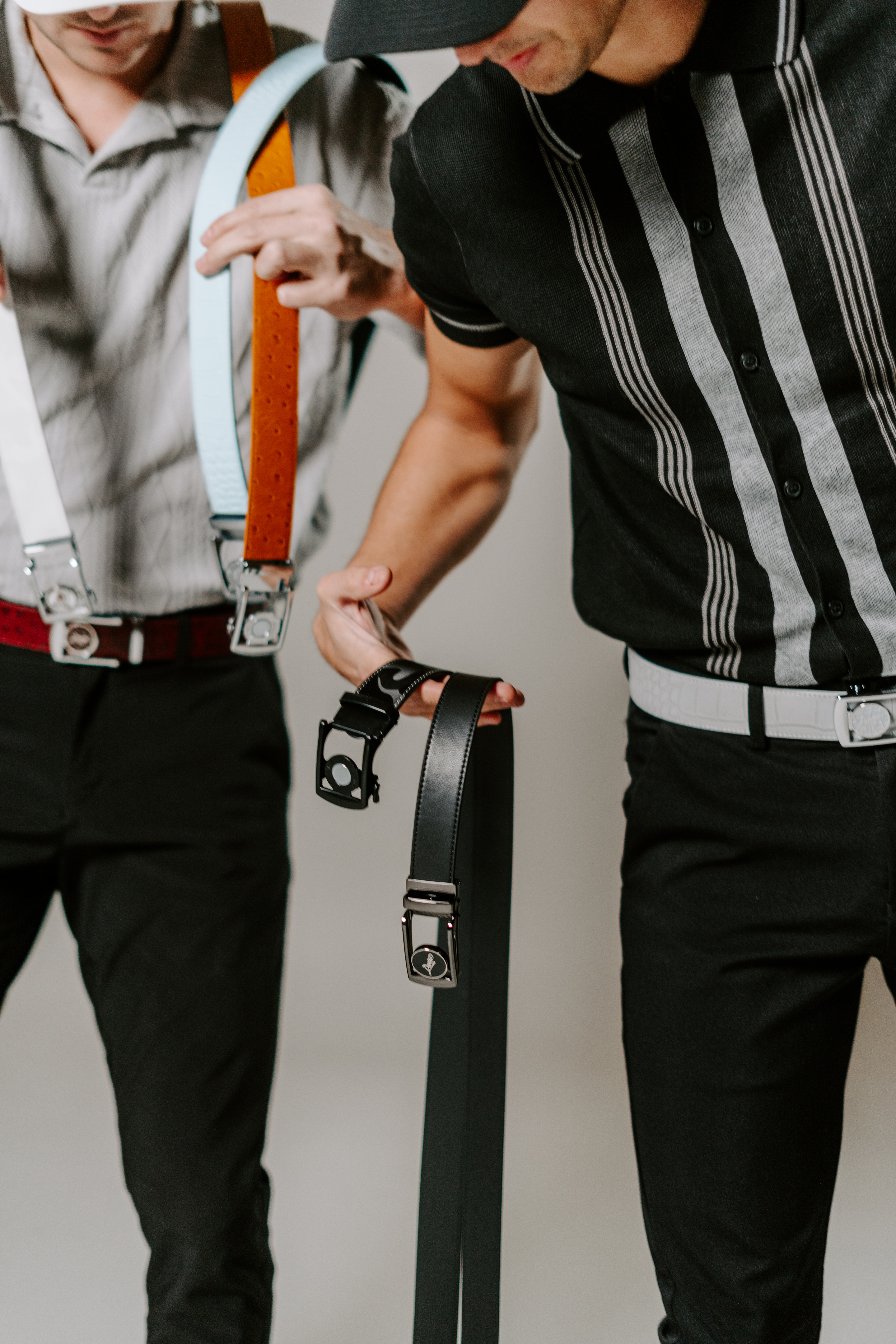 Two people holding belts, wearing striped shirts and suspenders.
