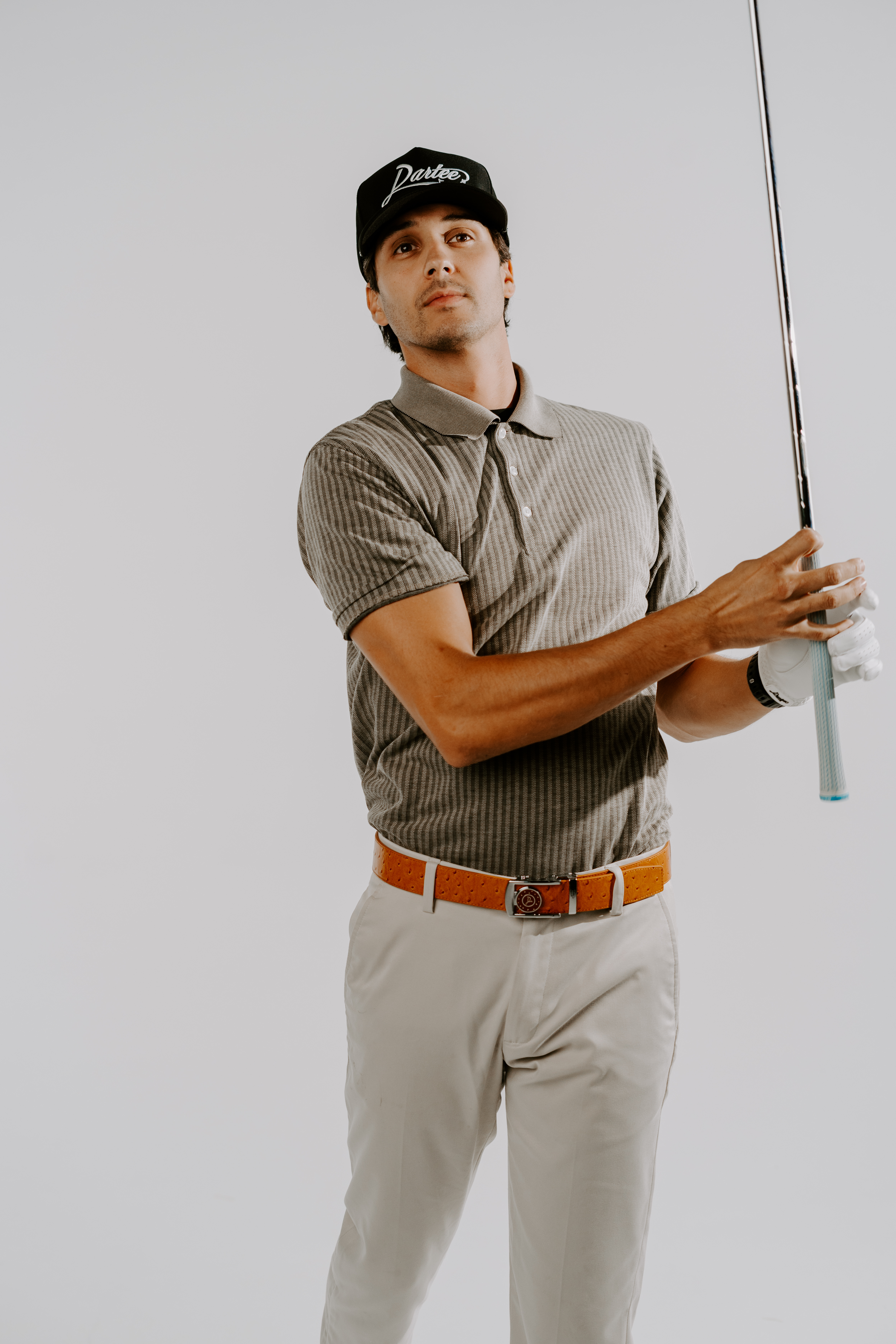 Person wearing a striped shirt and hat, holding a golf club against a plain background.